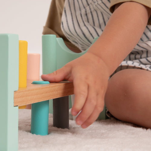 A child’s hand reaches for the TP Toys Owl & Fox Wooden Hammer Bench—an FSC® certified toy—on a white carpet, encouraging hand-eye coordination.