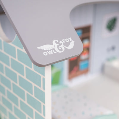 Close-up of the TP Toys Owl & Fox Wooden Dolls House—FSC® certified—with a grey roof edge, turquoise brick-patterned wall, and blurred interior, ideal for Montessori toy fans and pretend play accessories.