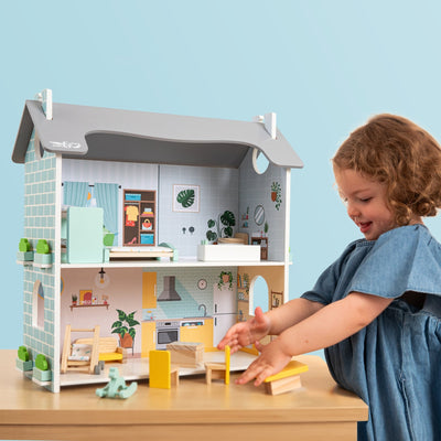 A young child smiles while playing with the Owl & Fox Wooden Dolls House by TP Toys, enjoying pretend play with its miniature accessories.