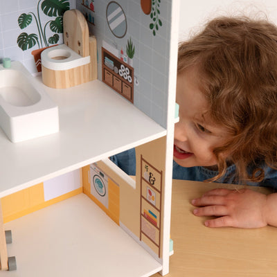 A young child smiles while exploring the TP Toys Owl & Fox Wooden Dolls House—FSC® certified—with painted bathroom and laundry room details, perfect Montessori toy pretend play accessories.