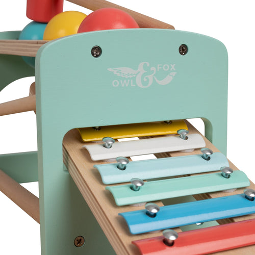 A close-up of the TP Toys Owl & Fox Wooden Xylophone Bench, an FSC® certified Montessori toy with metal keys and pastel colors, designed to develop fine motor skills and featuring the Owl & Fox logo on a mint-green panel.
