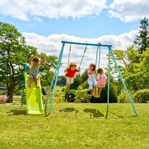 Four children enjoy the TP Toys TP Metal Swing Slide & Glide: one goes down the slide, one swings, and two share a swing. Trees and grass in the background enhance this lively garden playset scene.