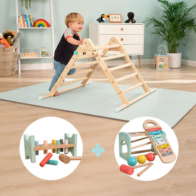 A child stands on a play mat, holding the TP Toys Energetic Play Pack: TP Active-Tots Pikler Style Climbing Triangle, with Owl & Fox Hammer Bench and Owl & Fox Xylophone displayed nearby.