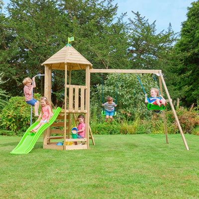 Five children play on the TP Toys Castlewood climbing frame with Double Wooden Swing Arm & 1.8m Wavy Slide—FSC® certified—set on a grassy lawn surrounded by trees.
