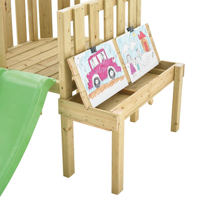 The TP Toys TP Forest Toddler Wooden Pink Quadpod Swing Set & Slide (FSC® certified) stands beside a wooden bench with two children’s drawings on the backrest.