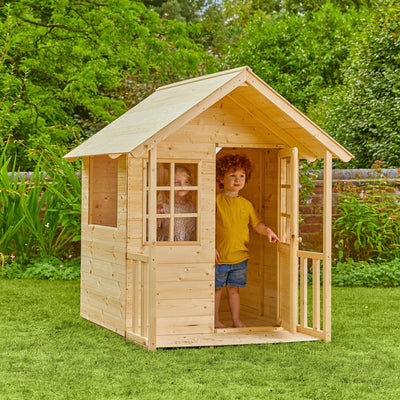 Two children play in and around the TP Toys Lavender Cottage Wooden Playhouse—FSC® certified—set on a grassy lawn, perfect for imaginative outdoor fun.