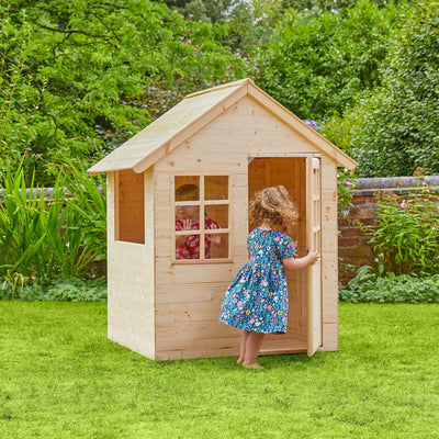 Two young children enjoy imaginative play around the TP Toys Foxglove Cottage Wooden Playhouse—FSC® certified—set on a grassy lawn among green plants and trees, making outdoor fun even more magical.