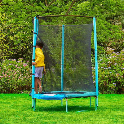 A child in a yellow jacket stands on a TP Toys UP 4.5ft Junior Trampoline with a zip-free IGLOO door and safety net in a green garden.