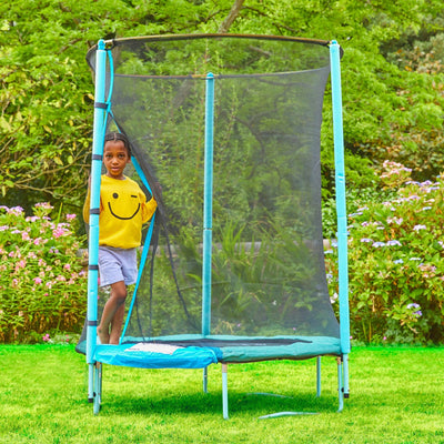 A child in a yellow smiley face shirt stands inside a blue TP Toys UP 4.5ft Junior Trampoline with zip-free igloo door and safety netting, set up on the grass in the backyard.