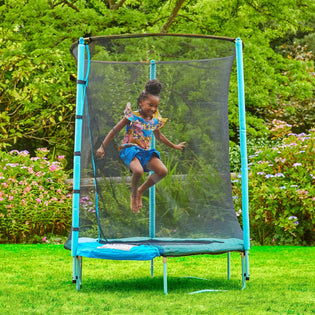 A young girl jumps on a TP Toys UP 4.5ft Junior Trampoline with safety netting and a zip-free IGLOO door in a grassy backyard garden.