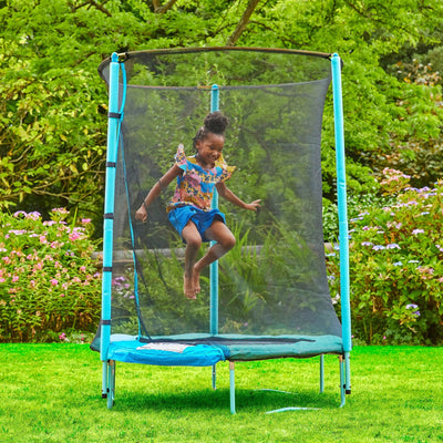 A young girl jumps on a TP Toys UP 4.5ft Junior Trampoline with safety netting and a zip-free IGLOO door in a grassy backyard garden.