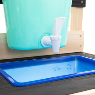 A close-up of the TP Toys TP Little Chef Wooden Mud Kitchen—FSC® certified—shows its turquoise container with white spout over a blue tray, ideal for outdoor mud kitchen play.