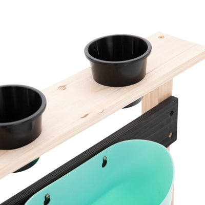 The TP Toys Little Chef Wooden Mud Kitchen, made from FSC® certified wood, features a sturdy stand with two black cups on top and a light blue container below—ideal for outdoor play or creative mud kitchen fun.