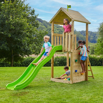 Four children enjoy the TP Skywood Wooden Play Tower by TP Toys—featuring a slide, climbing wall, and sandbox—in a grassy yard with trees. This modular tower is FSC® certified for sustainable outdoor fun.