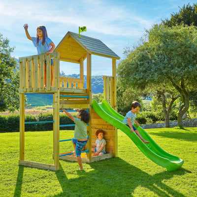 Four children play on the TP Toys TP Skywood Wooden Tower Climbing Frame with Ripple Slide & Sky Deck—made from FSC® certified wood—in a grassy area with trees and hills in the background.