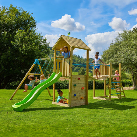 Children play on the TP Toys TP Skywood Wooden Tower Climbing Frame with Ripple Slide, Sky Bridge, Mini Tower & Double Swing Arm—an FSC® certified modular playset—on a grassy lawn under a cloudy blue sky.