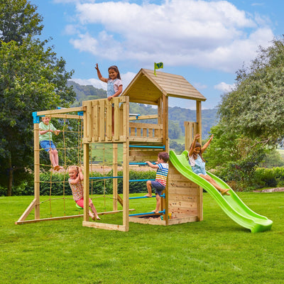 Five children play on a TP Toys TP Skywood Wooden Tower Climbing Frame with Ripple Slide, Sky Deck, Skyline & Flying Fox Add On (FSC® certified) in a grassy yard beneath a partly cloudy sky.