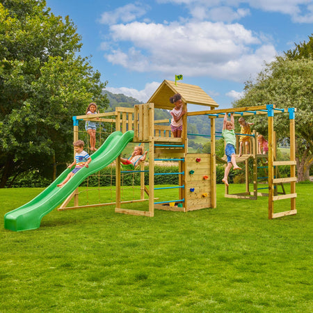 Six children play on the TP Skywood Wooden Tower Climbing Frame by TP Toys, featuring a Super Wavy Slide, Sky Deck, Monkey Bars, Skyline with Swing Seat & extra tower—FSC® certified—set on grass under a partly cloudy sky.