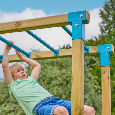 A child hangs from monkey bars on the TP Toys Skywood Wooden Climbing Frame, featuring two play towers, Sky Deck, Skyline with Flying Fox, swings, and super wavy slides—an FSC® certified outdoor playset.