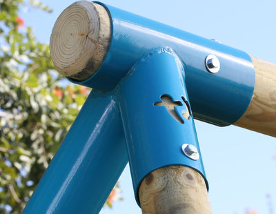 Close-up of a blue metal joint with bolts on the TP Toys TP Sherwood Wooden Double Swing—PEFC certified—connecting roundwood poles outdoors, with a tree and sky in the background.