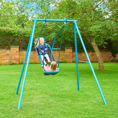 Two children play on the TP Toys TP Deluxe Single Metal Swing with Pirate Boat Seat in a grassy backyard, surrounded by trees and a brick wall.