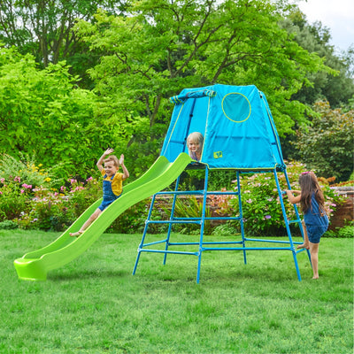 Three children play on the TP Toys TP Explorer Metal Climbing Frame Set & Ripple Slide with a blue tent in a grassy backyard surrounded by trees and flowers.