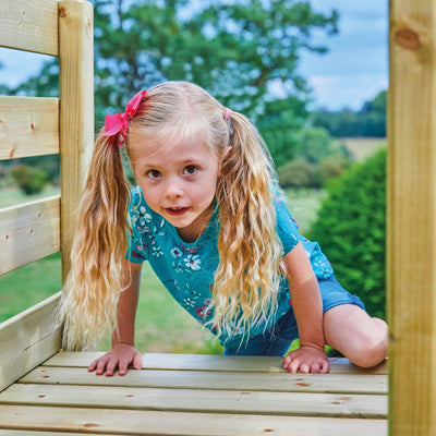 A young girl with long blonde pigtails and a pink bow plays outdoors on the TP Toys TP Robin Swing and 6ft Slide Set.