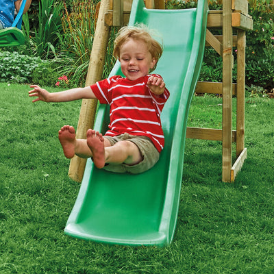 A young child with blond hair, dressed in a red striped shirt and khaki shorts, slides down the green 6ft slide of the TP Toys TP Robin Swing and 6ft Slide Set in a grassy backyard.