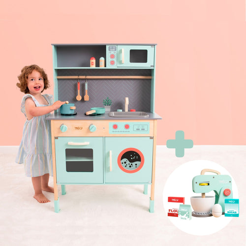 A young child stands beside the TP Toys Owl & Fox Wooden Imagination Kitchen & Baking Set (FSC® certified), with cookware, food props, and a toy mixer with accessories for creative pretend play.