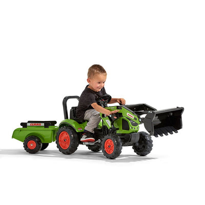A young child rides a TP Toys Falk Class Backhoe with Trailer, wearing a dark shirt and gray pants.