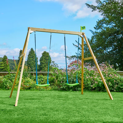 The TP Toys TP Forest Wooden Double Swing—FSC® certified, featuring Rapide Swing Seats and crafted from premium pine, stands on a lawn with trees and flowering bushes in the background.