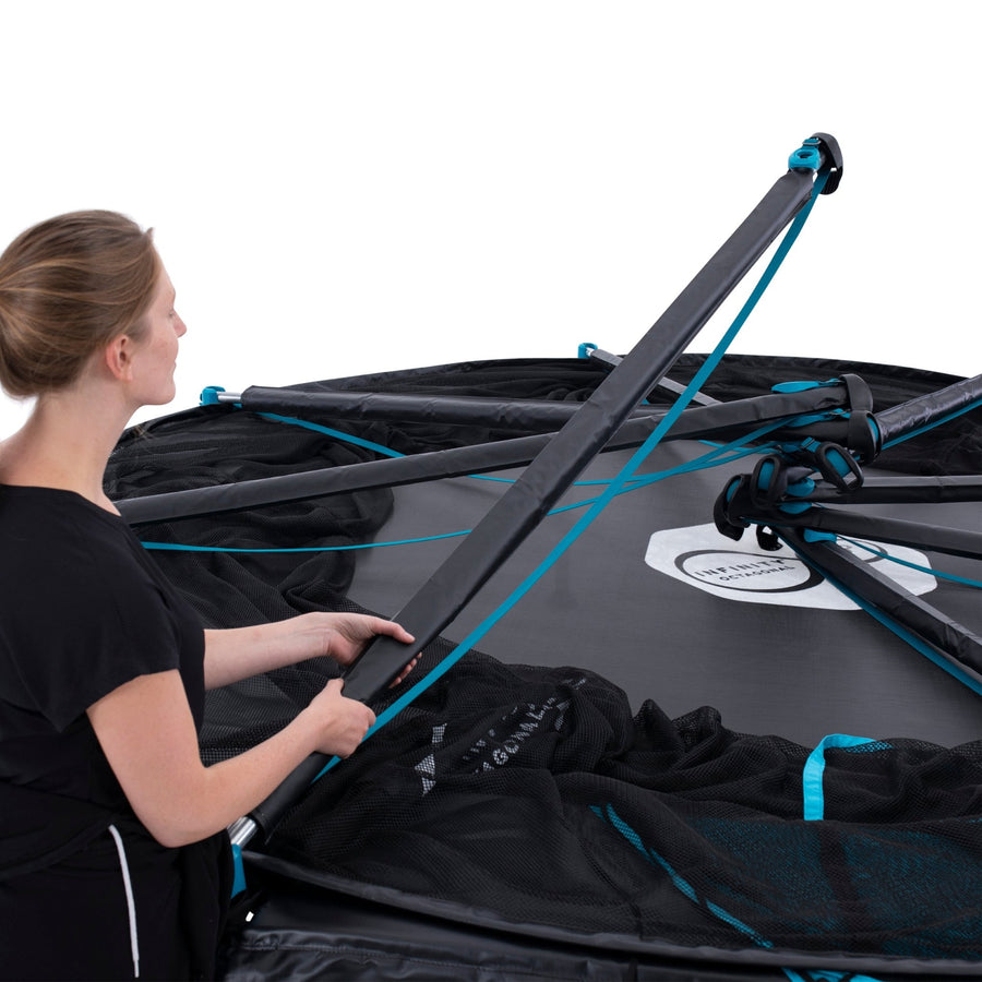 A woman assembles the TP Toys Infinity Octagonal 12ft Trampoline, attaching black and blue poles to the frame and safety net for a safe bounce.