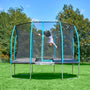 A person is mid-flip on the TP Challenger® 8 ft Trampoline by TP Toys, featuring a patented SurroundSafe enclosure, outdoors on green grass with trees and a blue sky in the background.