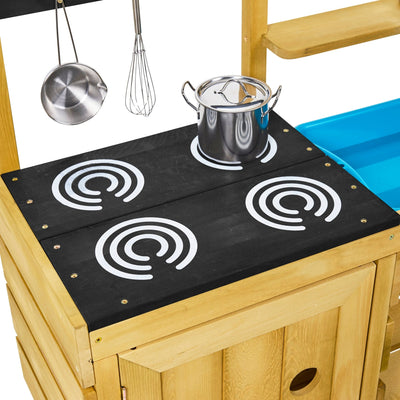 The TP Toys TP Junior Chef Wooden Mud Kitchen features a black stovetop with four burners, silver pot, hanging utensils, and wooden cabinetry—all crafted from FSC® certified wood for safe, eco-friendly play.
