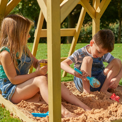 A boy and girl play in sand beside the TP Toys Build Your Own TP Treehouse Wooden Play Tower, FSC® certified.