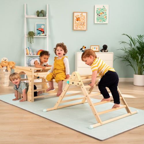 Four young children play on the TP Toys Active-Tots Pikler Style Wooden Climbing Triangle, Cube & Slide (FSC® certified) in a bright indoor space filled with plants, books, and colorful wall art.