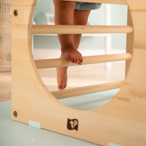 A child’s bare feet climb on the TP Toys TP Active-Tots Pikler Style Wooden Climbing Triangle, Cube & Slide—an FSC® certified Montessori toy—featured in a cozy indoor play area.