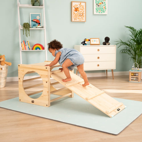 A toddler climbs the Active-Tots Pikler Style Two Climbing Cubes & Bridge by TP Toys in a bright, pastel-themed playroom, surrounded by Montessori toys and playful decor.