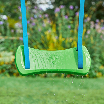 A green plastic swing seat with blue ropes, slick with water droplets, hangs from a TP Toys TP Knightswood Double Wooden Swing Set outdoors amid blurred greenery and flowers.