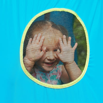 A young child smiles and peeks through the mesh window of the bright blue TP Toys TP UFO Den & Metal Frame, playfully covering part of their face with their hands.
