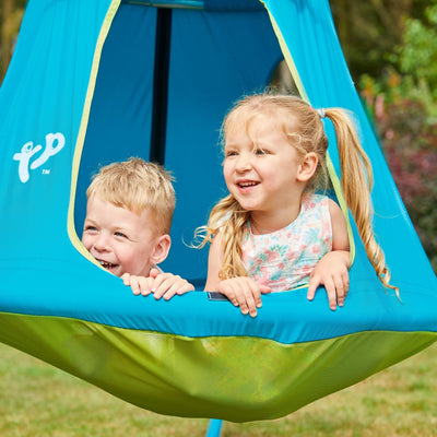 Two young children smile from the opening of the TP UFO Den & Metal Frame by TP Toys, enjoying hours of outdoor play together inside this blue and green hanging tent.