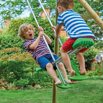 Two young children play outdoors on the TP Kite Wooden Double Swing Set with 8ft Slide by TP Toys. Both wear striped shirts and shorts, and one child looks excited as they enjoy the slide and climbing features.