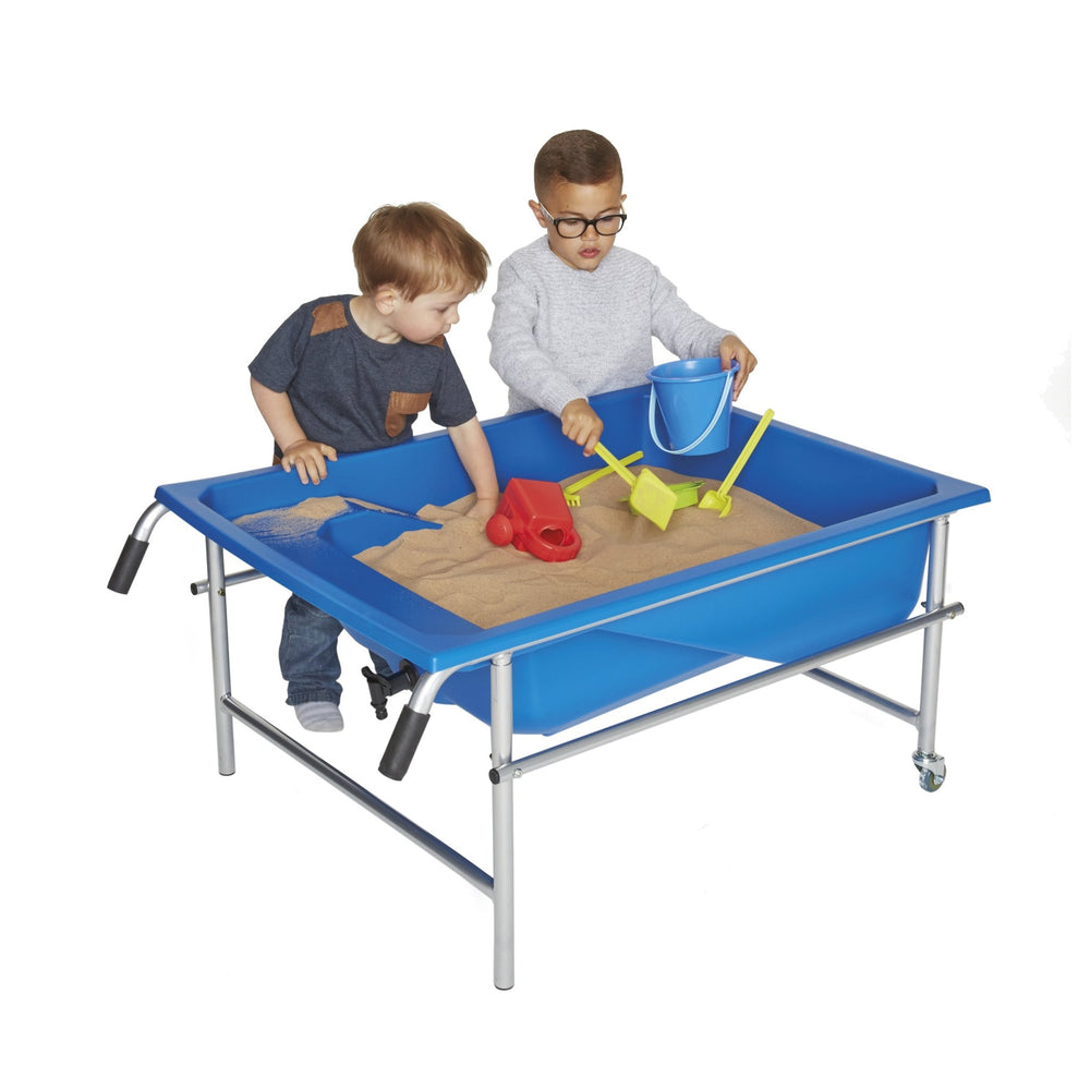 Two young children play with sand and educational toys in the TP Toys Oasis Blue Tray—a portable sensory table on a sturdy metal frame with wheels.